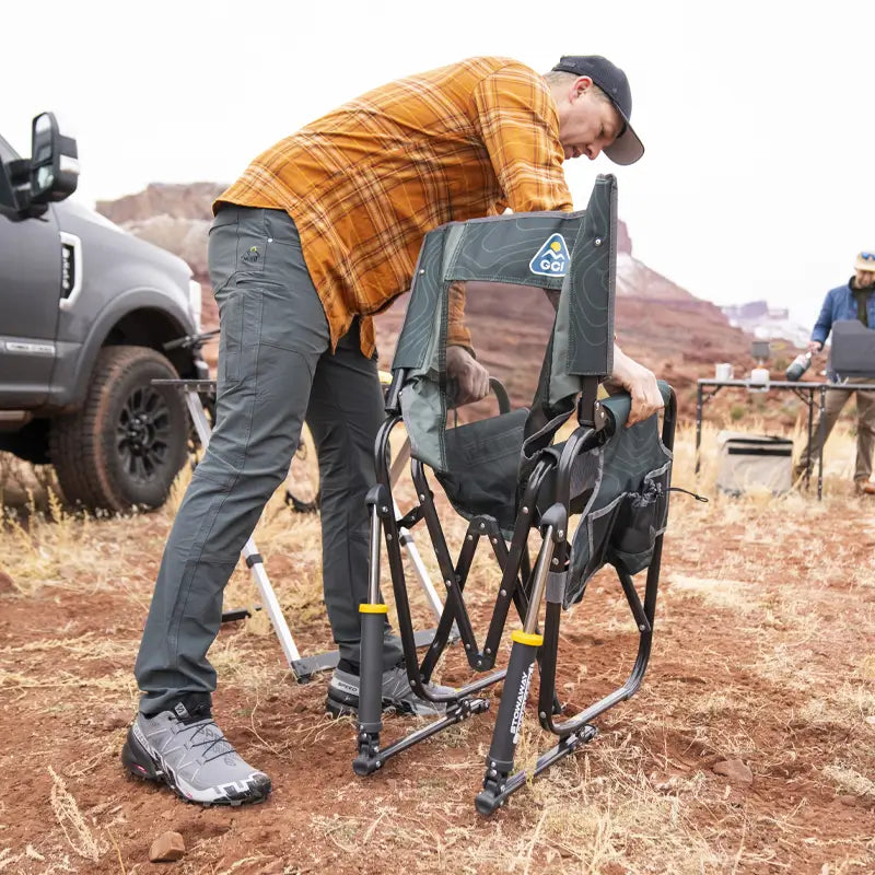 Man unfolding the hunter topo Stowaway Rocker at a campsite with red rock formations.