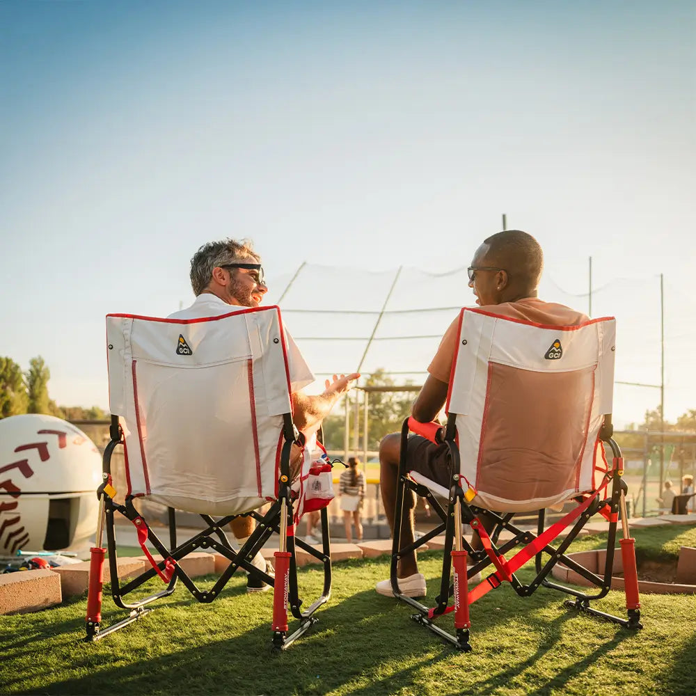 Two men sitting in a stowaway rocker baseball print next to a baseball field.