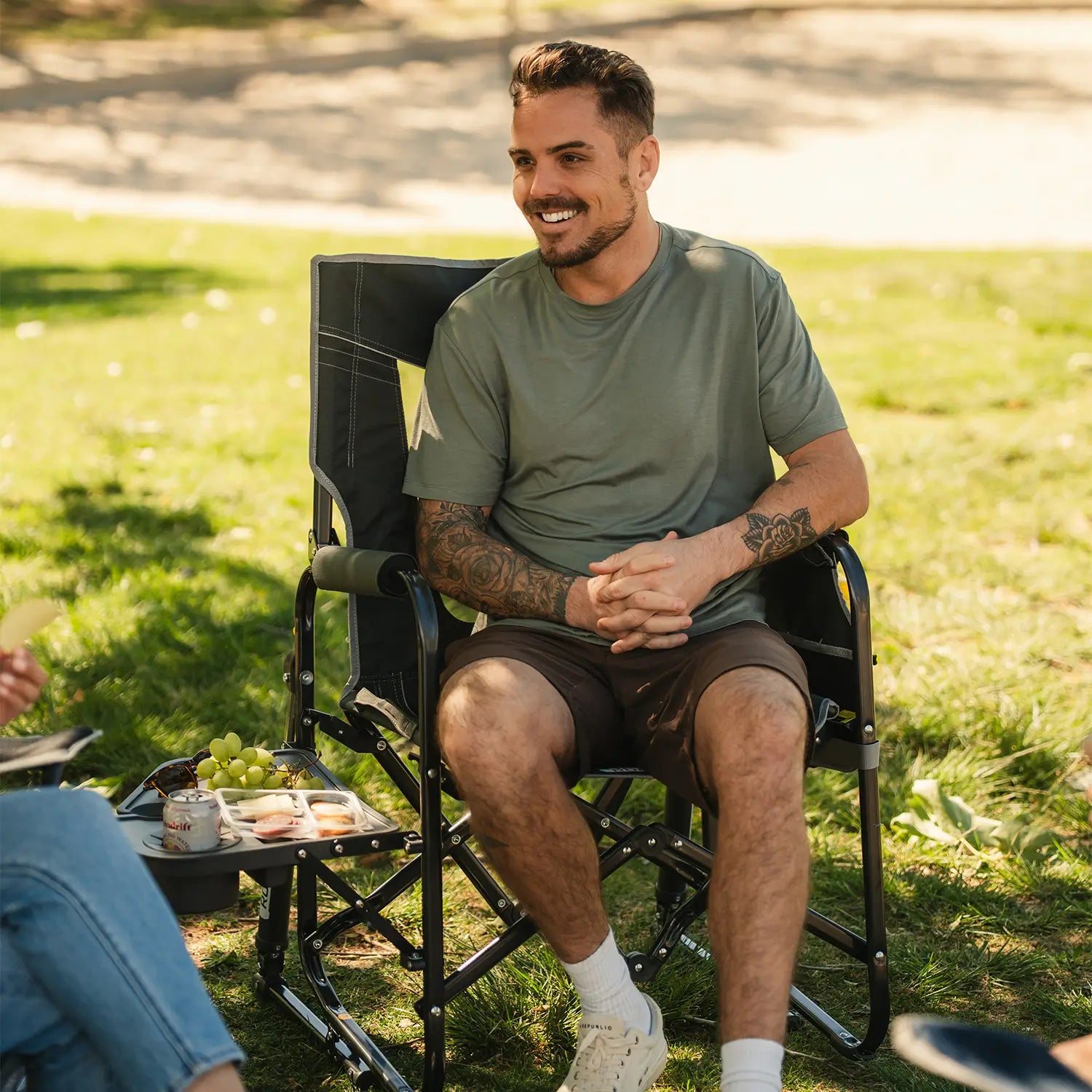 A man smiling and laughing while sitting in a Stowaway Rocker with Side Table at a park.