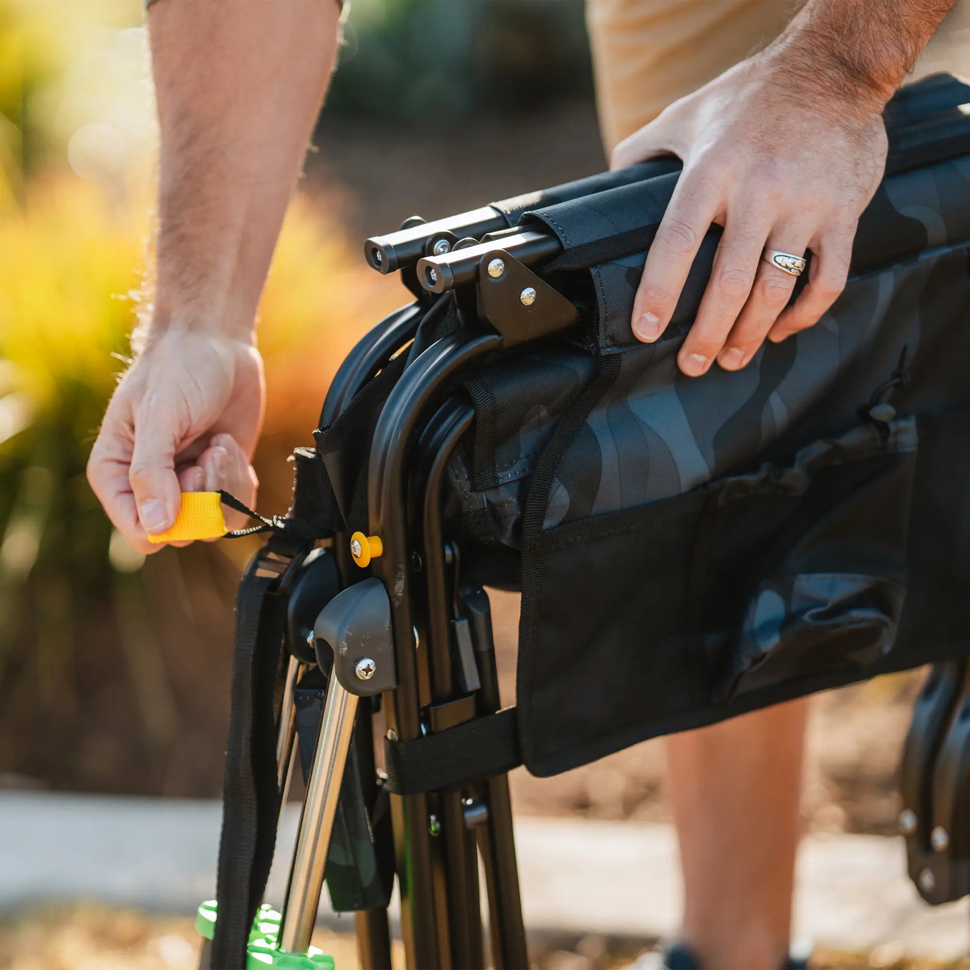 Close-up of hands unfolding the stealth camo Stowaway Rocker by pulling the yellow release strap.