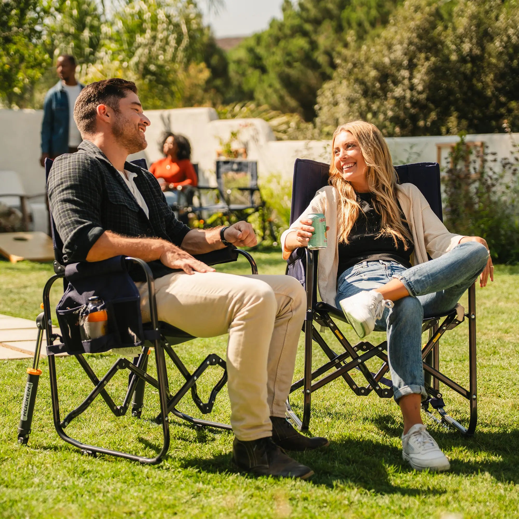 Two people sitting and laughing in a tailgater rich blue Stowaway Rocker in a backyard setting.