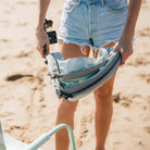 Woman holds folded pastel green sunshade accessory at the beach, showing its compact design.
