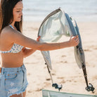 Woman in a bikini unfolds the pastel green sunshade to attach it to her beach chair.