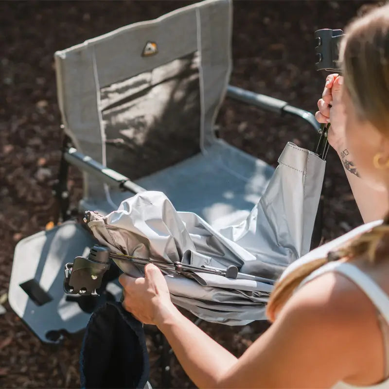 Woman unfolds an Indigo SunShade Accessory in front of a grey outdoor chair.