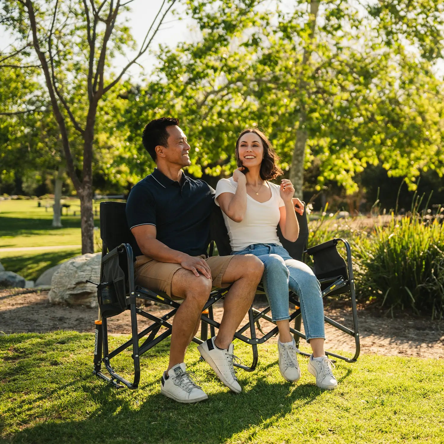 A couple sitting together on a Tandem Rocker while at a park.
