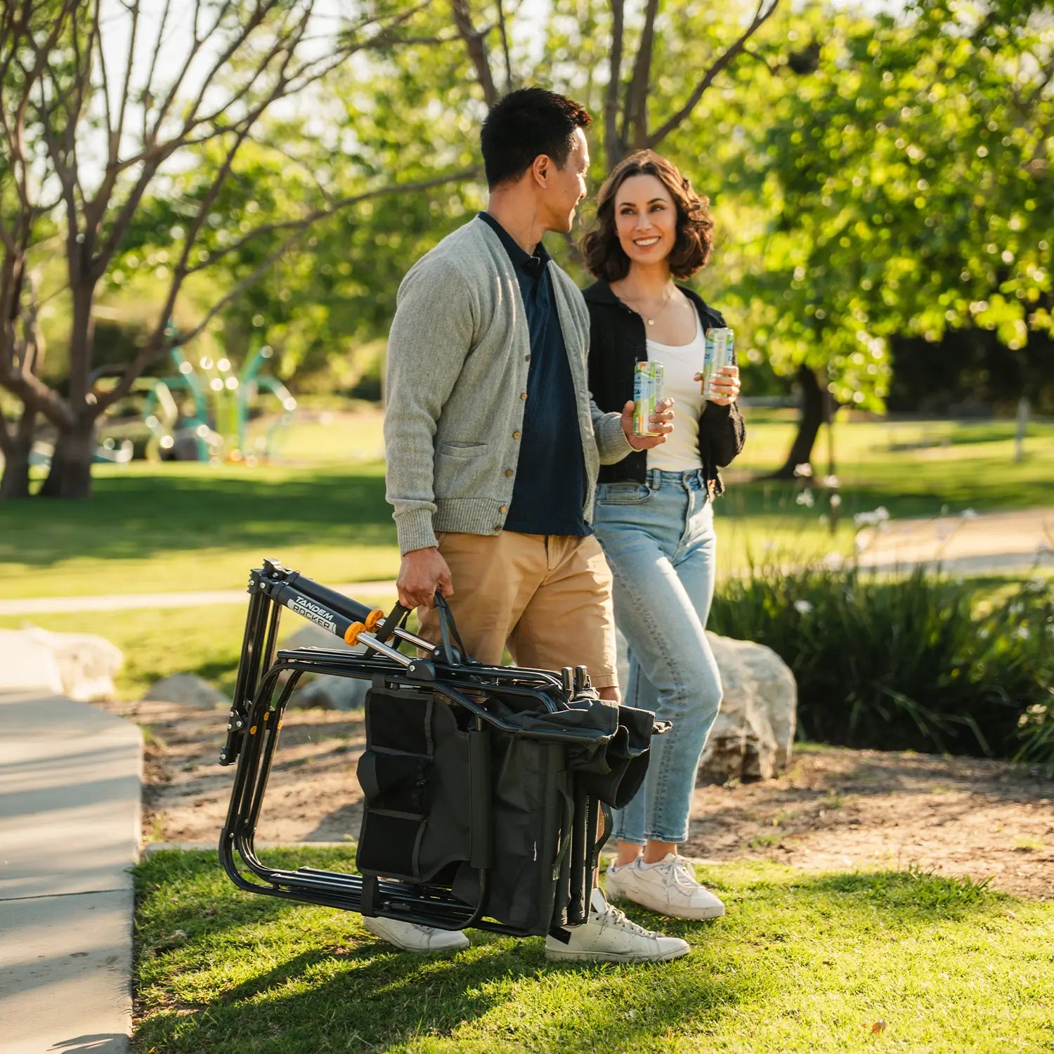 A man carrying a Tandem Rocker by the carry strap as he walks with a woman at a park.