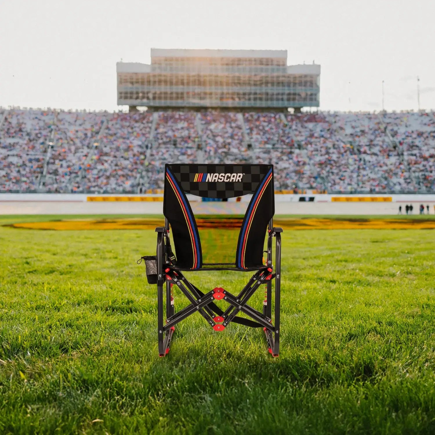 An Adjustable Rocker NASCAR chair sitting on a patch of grass in front of a racecar track.