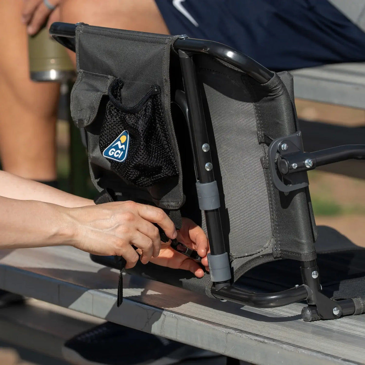 Close-up of hands securing the underside strap on a dark charcoal Big Comfort Stadium Chair with Armrests 2.0.