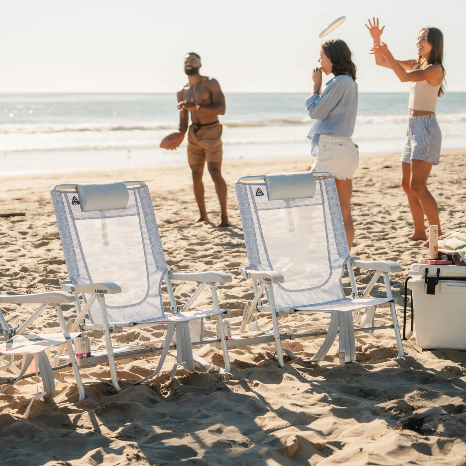 Two GCI Big Surf chairs in light blue mosaic set up near a cooler, with three people playing frisbee in the background.