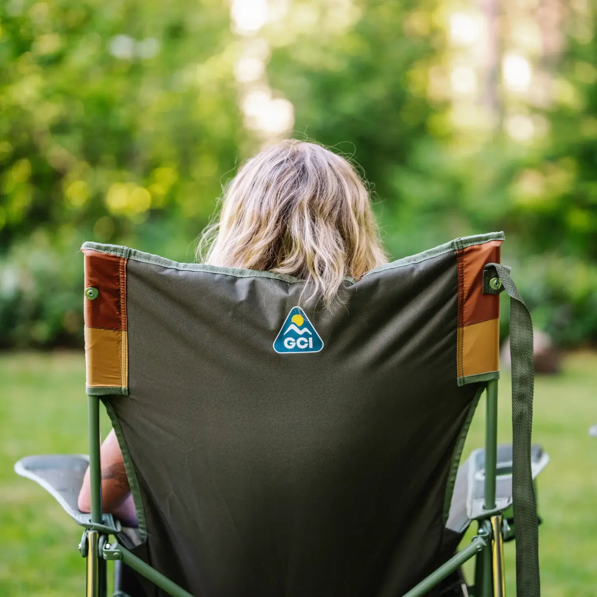 Back view of a woman seated in an olive Comfort Pro Insulated Rocker, with GCI logo visible on the backrest.