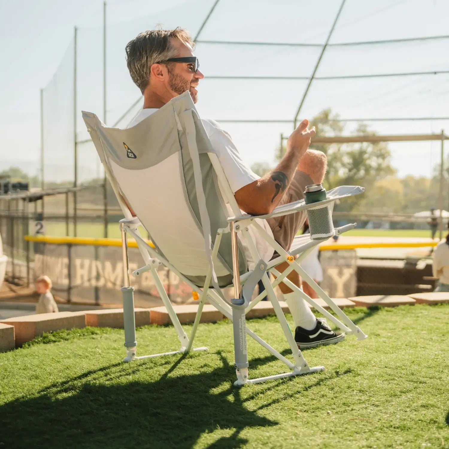 Man relaxing at a softball field in a GCI Outdoor Comfort Pro Rocker XL in Heathered Light Blue, right side view.