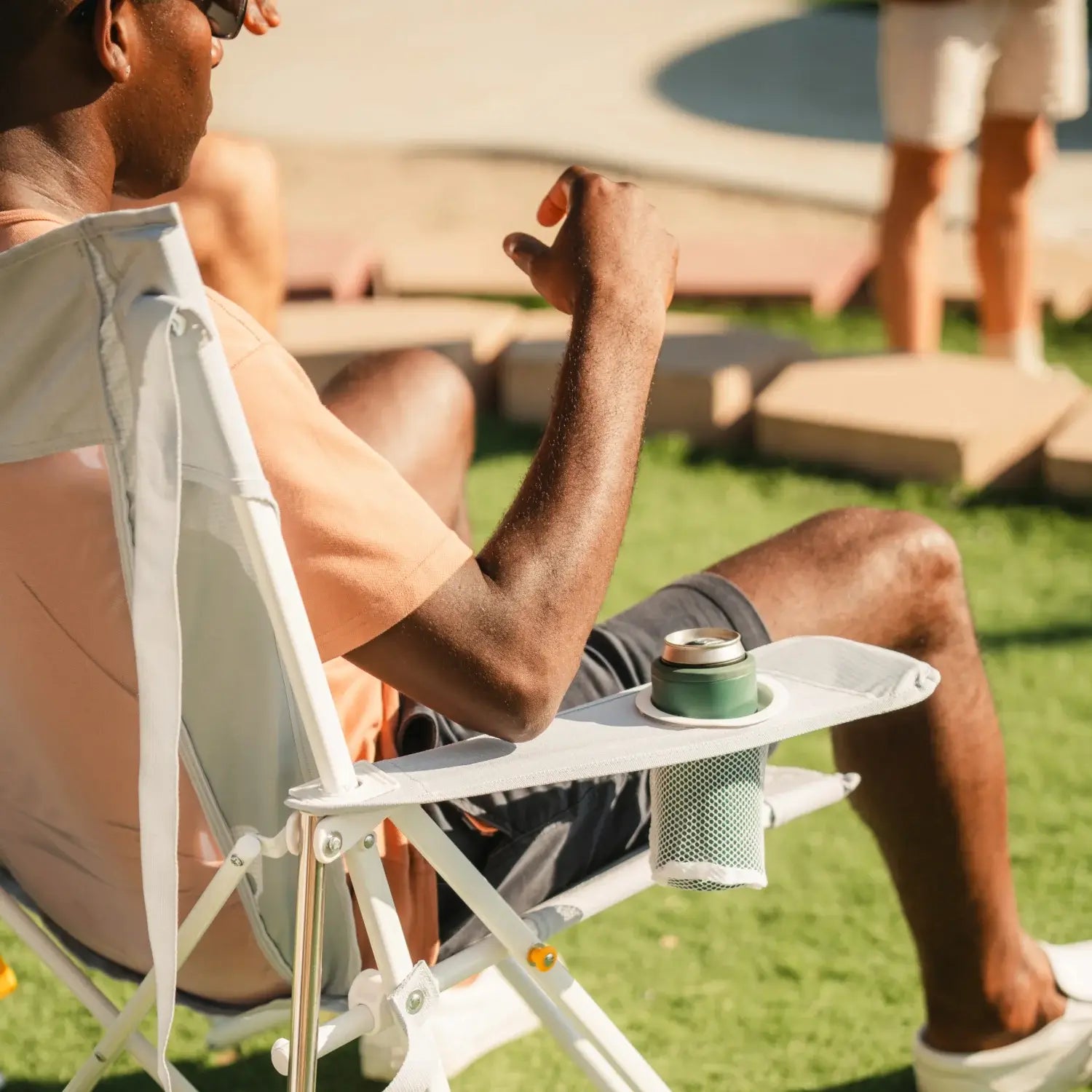 Close-up of a man relaxing in a GCI Outdoor Comfort Pro Rocker XL in Heathered Light Blue, highlighting the armrest cup holder, rear left angle view.