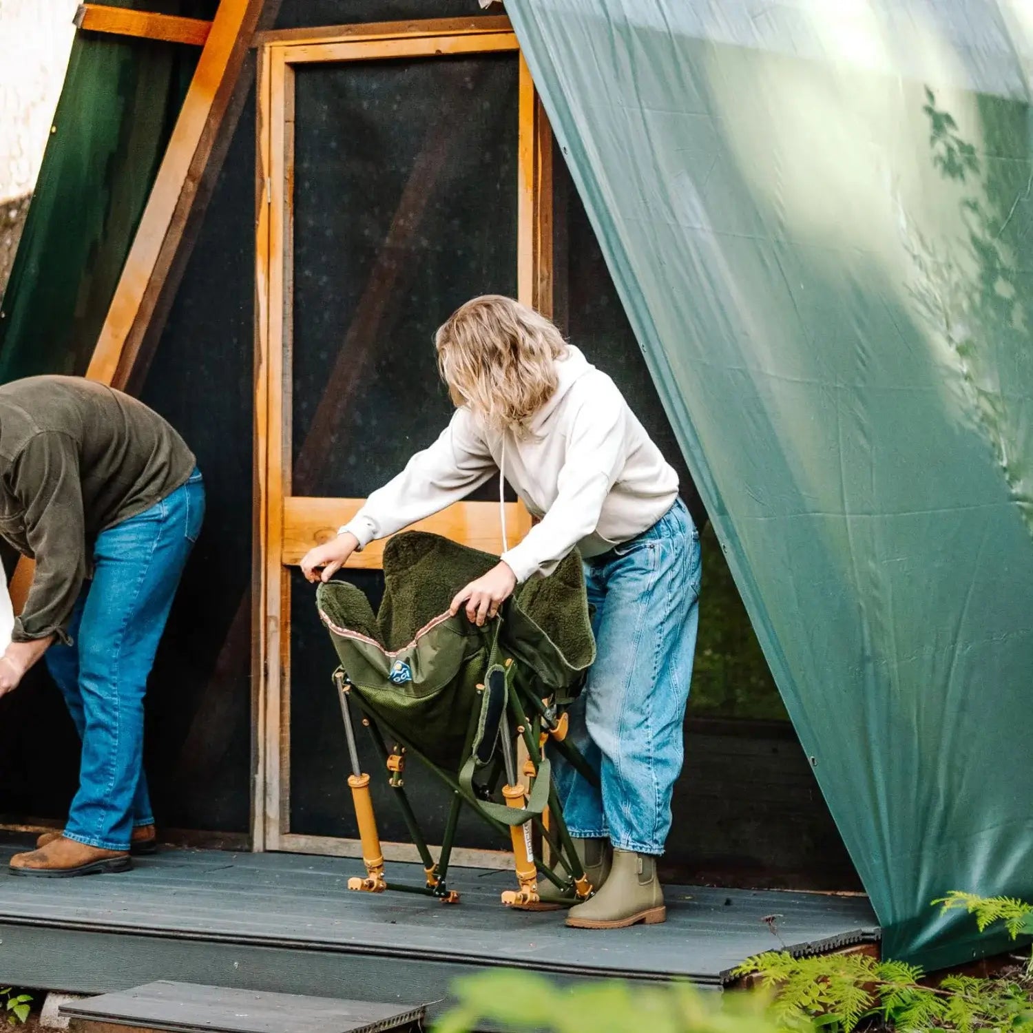Woman sets up an olive Fleece Rocker on a wooden deck outside an A-frame cabin, with a man standing nearby.