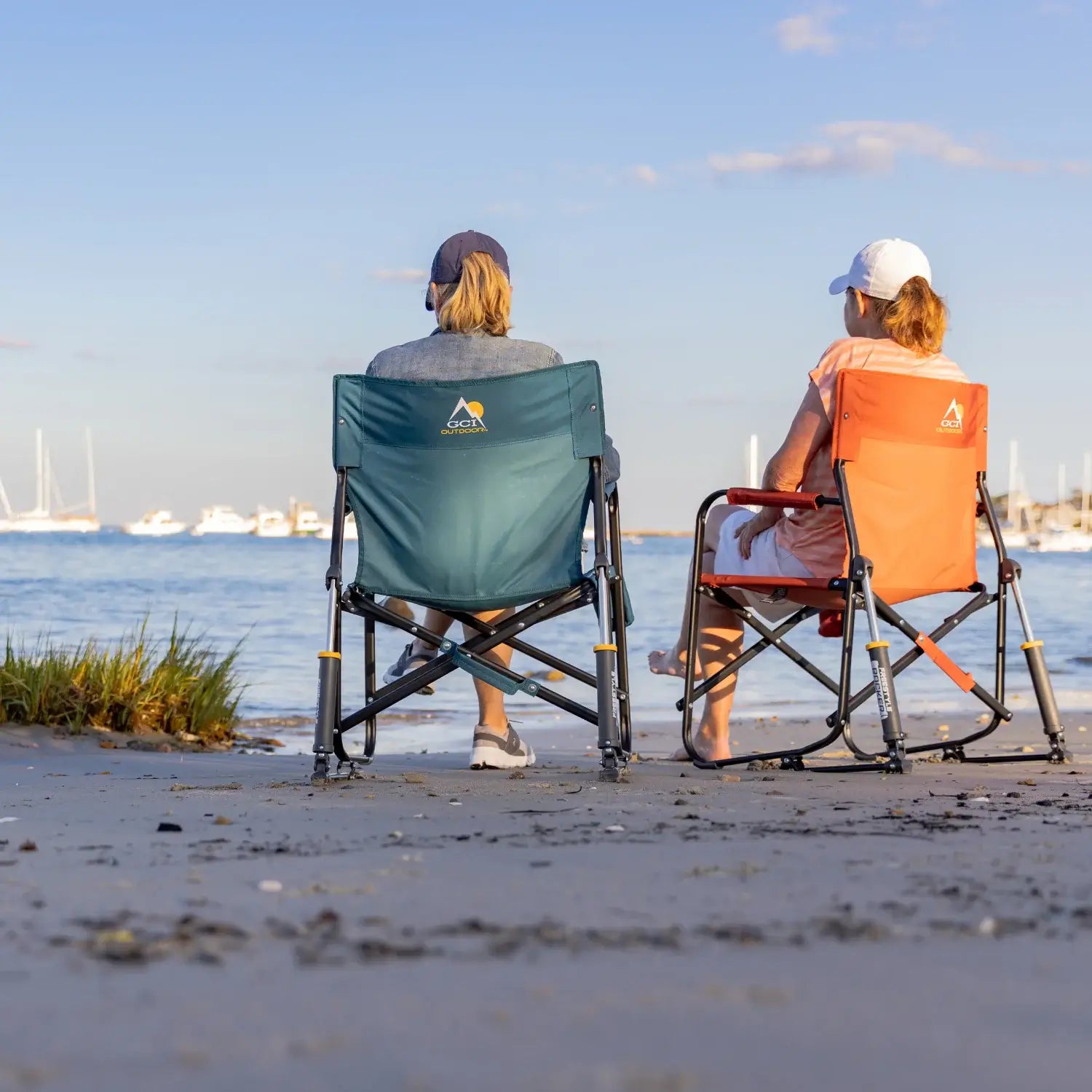 Two women sitting in freestyle rockers facing the water with sailboats in the distance.