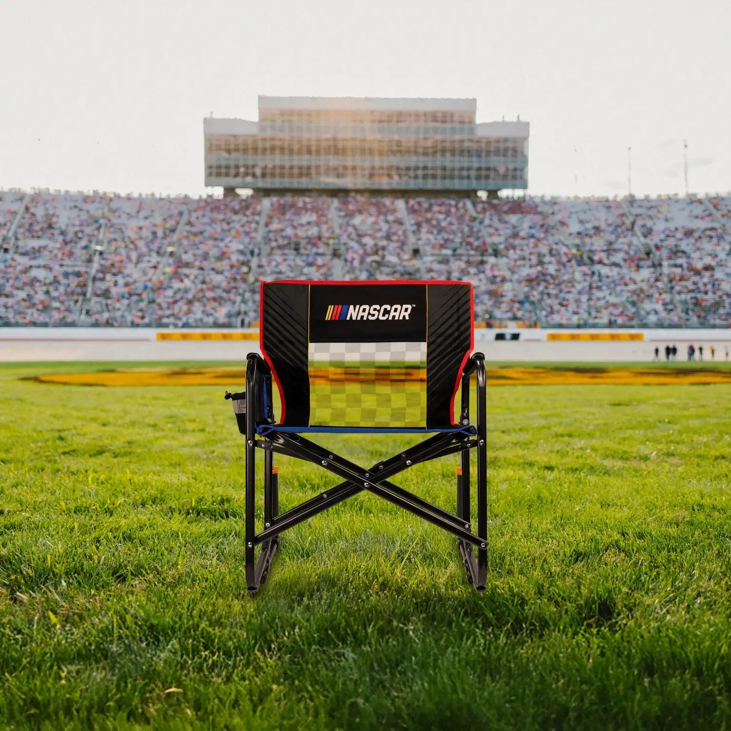 A Freestyle Rocker XL NASCAR chair sitting on a patch of grass in front of a racecar track.