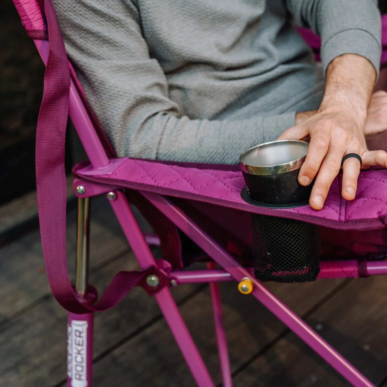 Close-up of a hand resting on the armrest of a berry Kickback Insulated Rocker, with a metal cup set in the built-in cup holder.