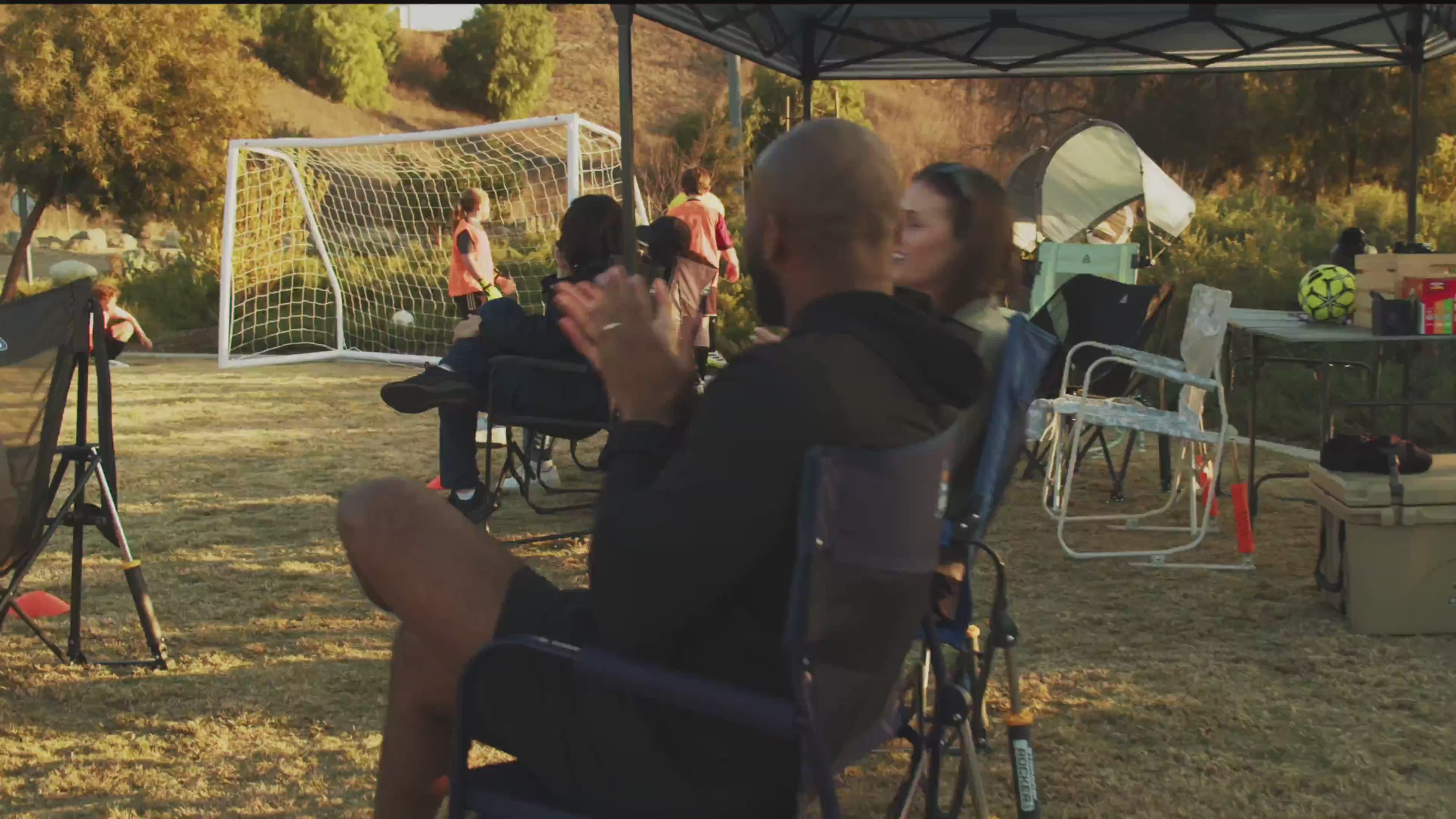 Two adults rocking in a Stowaway Rocker while clapping at a soccer game.