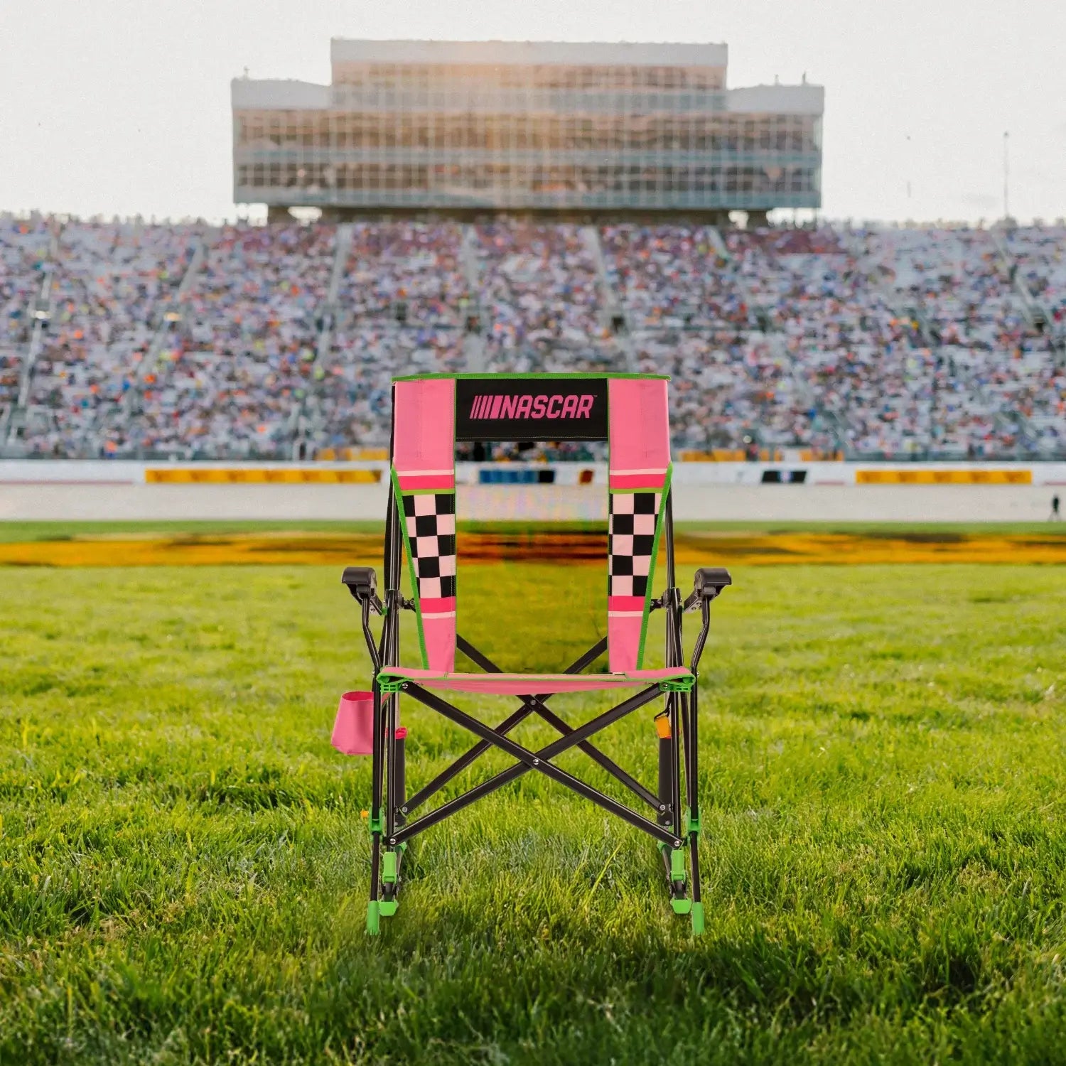 A Roadtrip Rocker NASCAR chair sitting on a patch of grass in front of a racecar track.