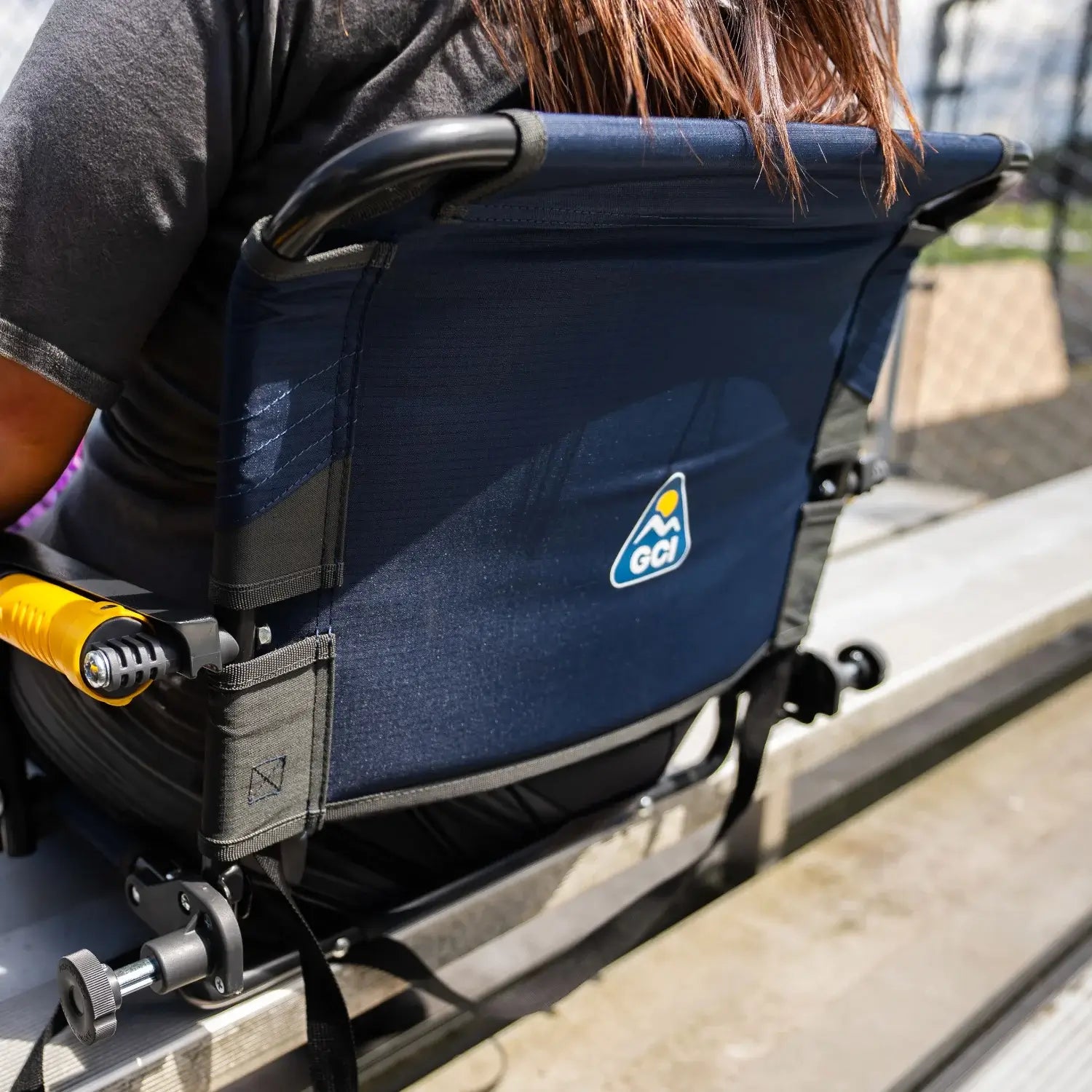 Close-up of the back of an indigo Stadium Rock-Cliner 2.0, showing the logo patch and bracket clamps securing it to bleacher seating.