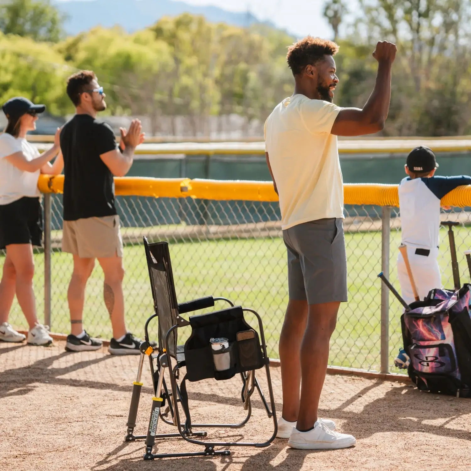 Man standing and cheering at a baseball game next to a black stowaway rocker.