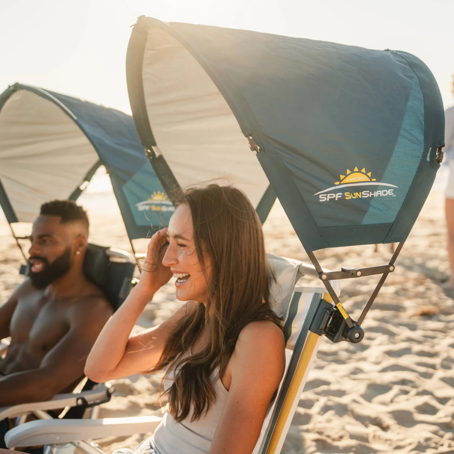 Woman relaxing in a beach chair with a teal GCI Outdoor SPF SunShade Accessory, with a man lounging beside her under a matching sunshade.