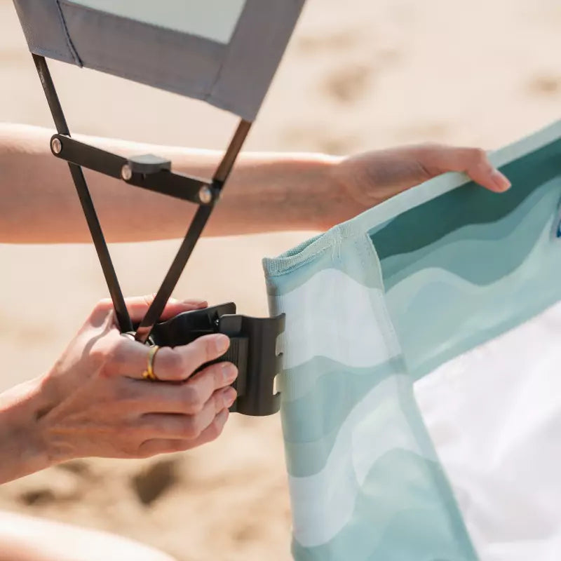 A person attaches a sunshade to a light green beach chair, highlighting the sunshade's adjustable and easy-to-use design.