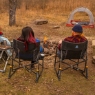 Two people sitting next to a bonfire sitting in a black freestyle xl chair. 
