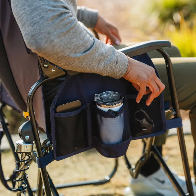 A seated person accesses the built-in side organizer of the Adjustable Rocker, storing a tumbler, phone, and keys.
