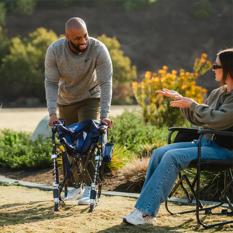 A man unfolds the Adjustable Rocker chair while smiling and talking to a woman seated nearby outdoors.