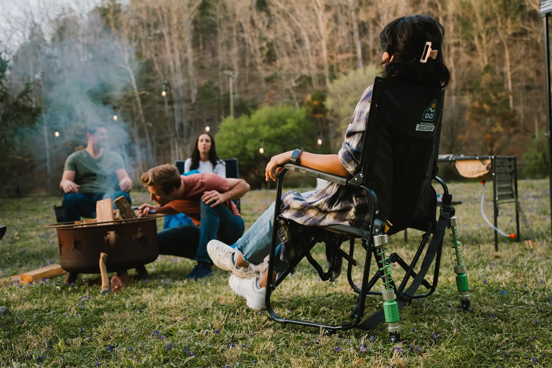 A woman sitting in an adjustable rocker next to a group surrounding a firepit. 