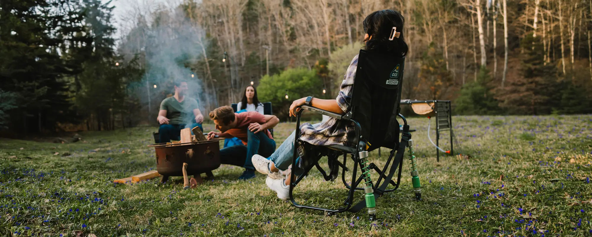 A woman sitting next to a bonfire while in an adjustable rocker chair. 