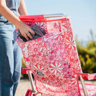 Woman placing a towel in the back pocket of a pink floral Backpack Beach Chair.