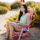 Woman sitting in a pink floral Backpack Beach Chair, smiling with flowers in the background.