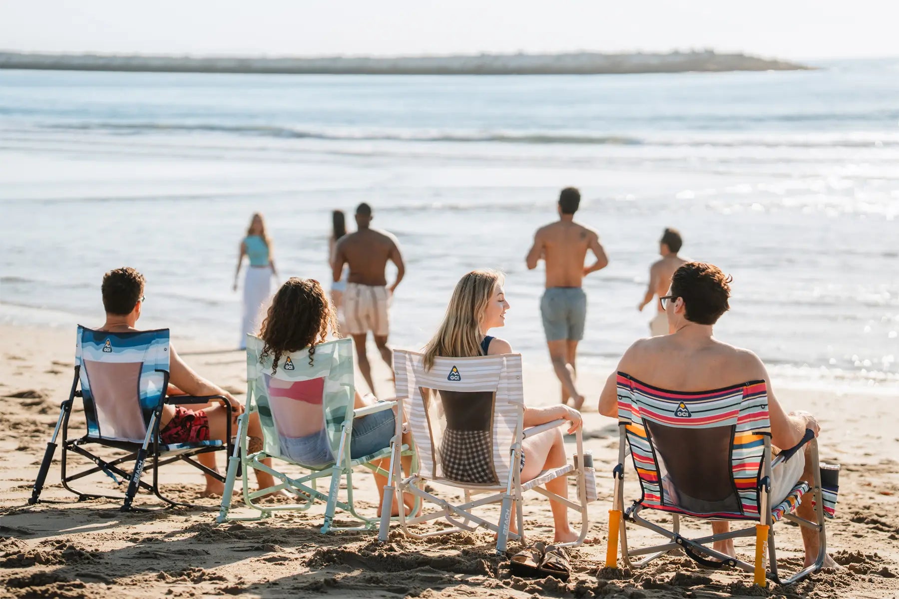 Friends lounge on beach rockers while others head to the ocean.