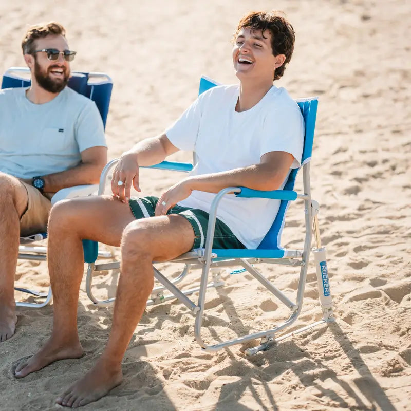 Two men relaxing barefoot on the beach in Saybrook Blue Beach Rocker chairs, smiling and enjoying the sunny weather.