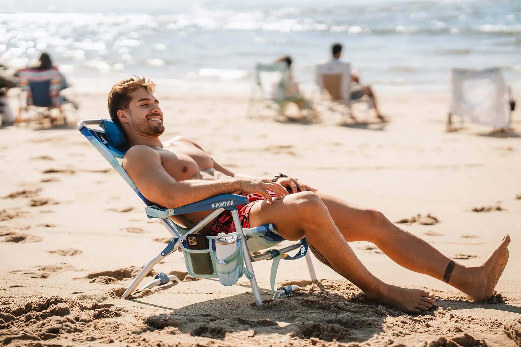 A shirtless man reclined on the Bi-Fold Beach Chair while relaxing on the beach. 