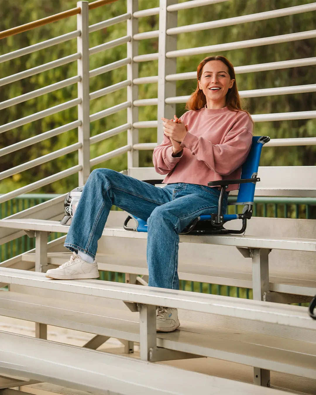 A woman cheering on a game while she sits in the bleachers with her big comfort stadium chair. 