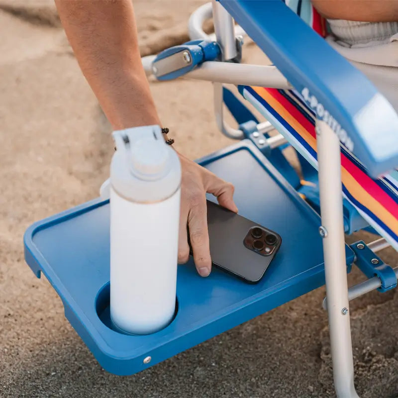 Close-up of a hand placing a phone on the blue slide table of a Big Surf chair, with a water bottle in the cup holder.