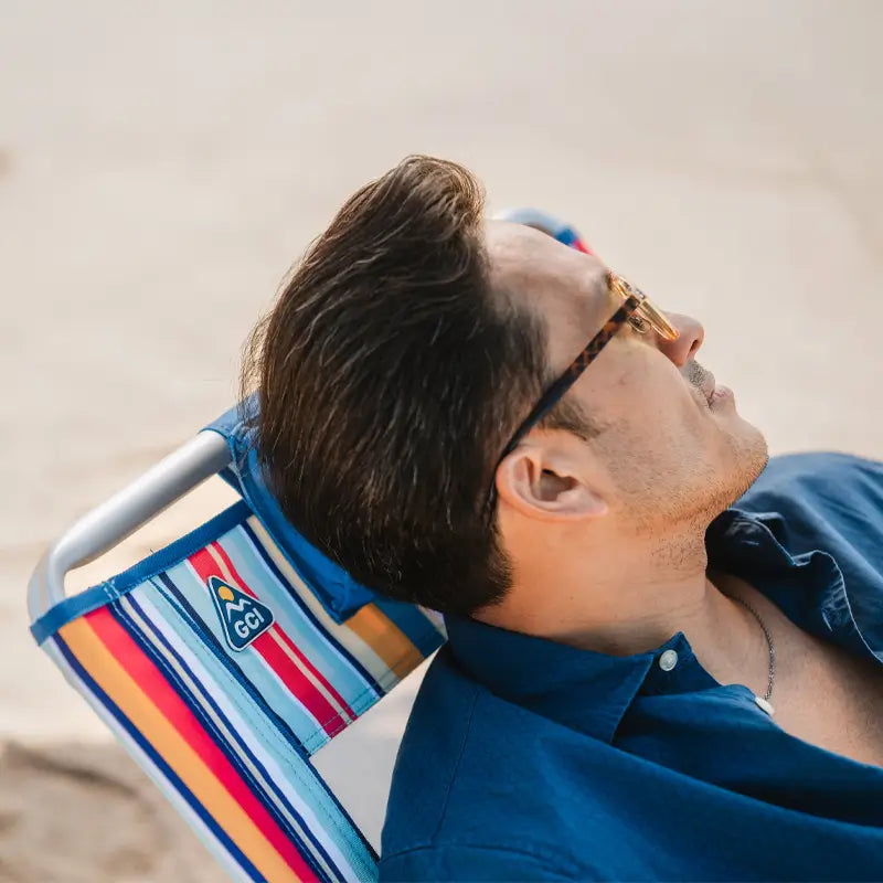 Man reclining in a Big Surf chair with colorful stripes and a GCI logo, wearing sunglasses and looking relaxed.