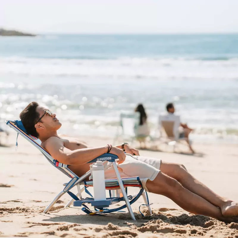 Man sitting in a Big Surf chair on the beach, holding a drink while chatting with a woman nearby.