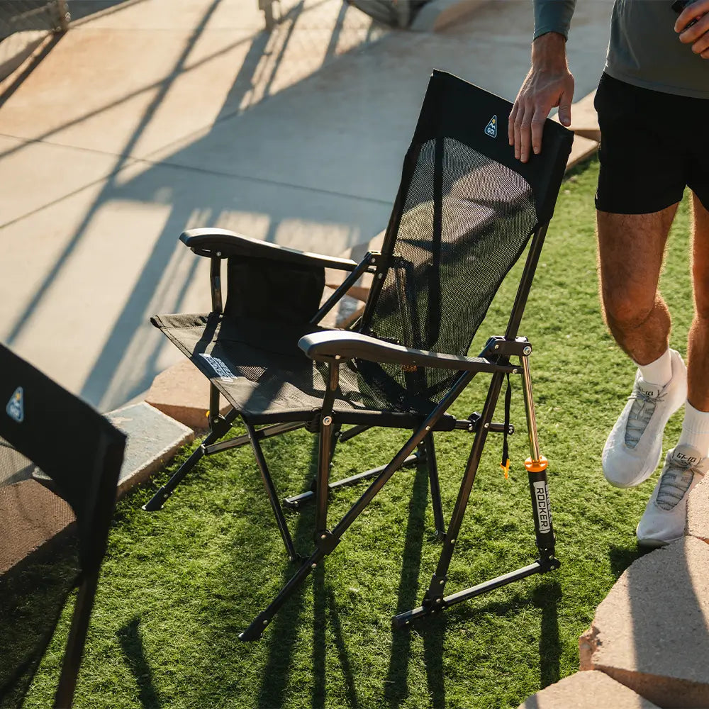 Person touching the folded Black Breeze Rocker by backrest near a baseball field.