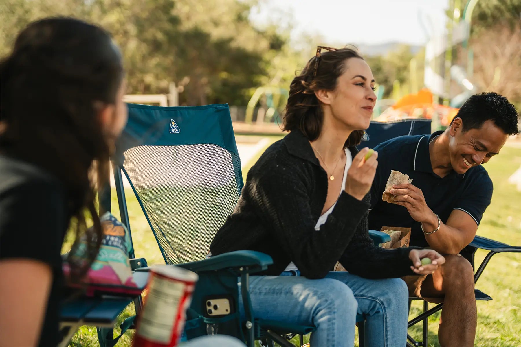 A group sitting together near a playground as they enjoy snacks that are on the Compact Camp Table 20.