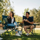A couple enjoying snacks at a park while they sit in their Comfort Pro Rocker and BreezeRocker. 
