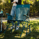 A full view of the teal BreezeRocker as a woman stands behind the chair. 