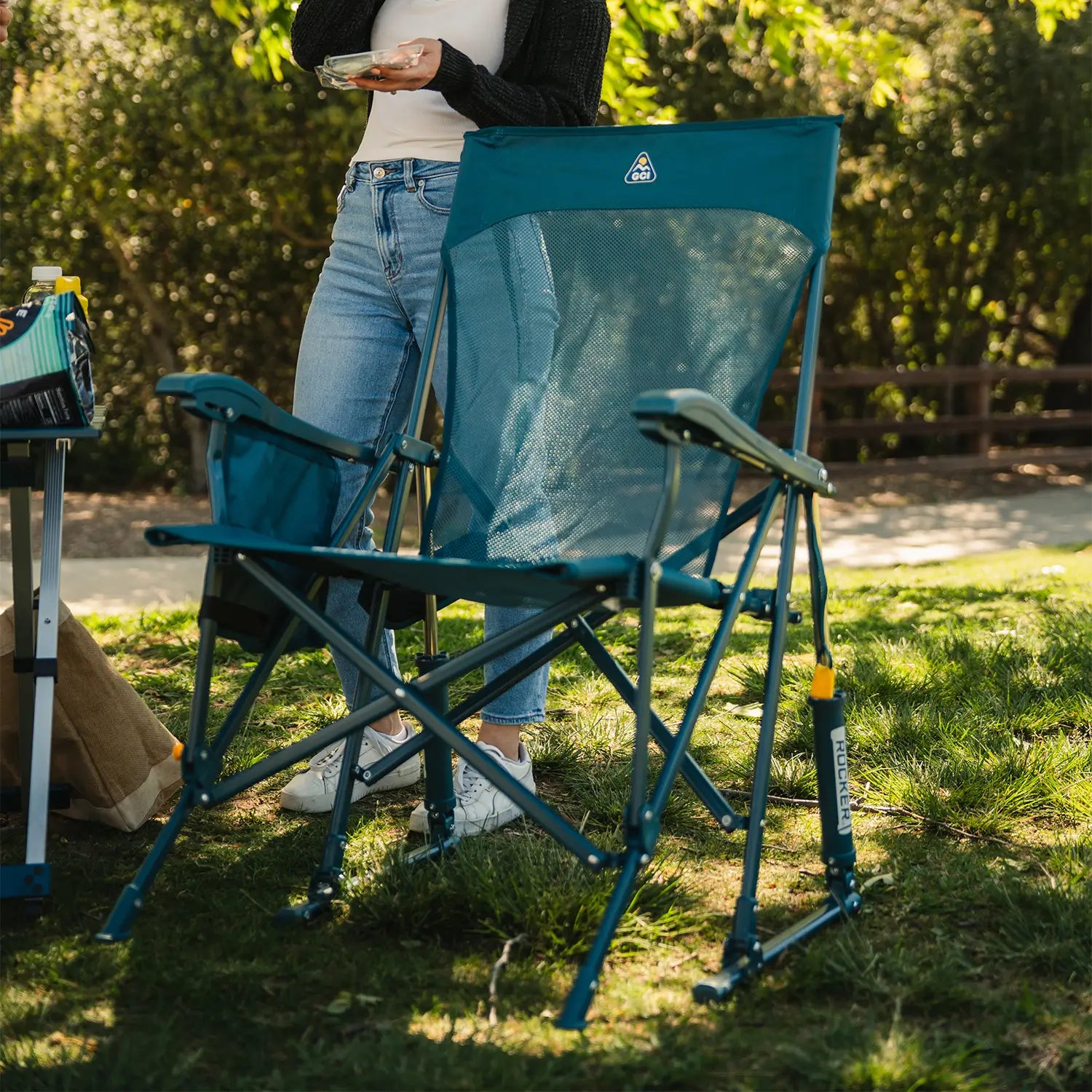 A full view of the teal BreezeRocker as a woman stands behind the chair. 