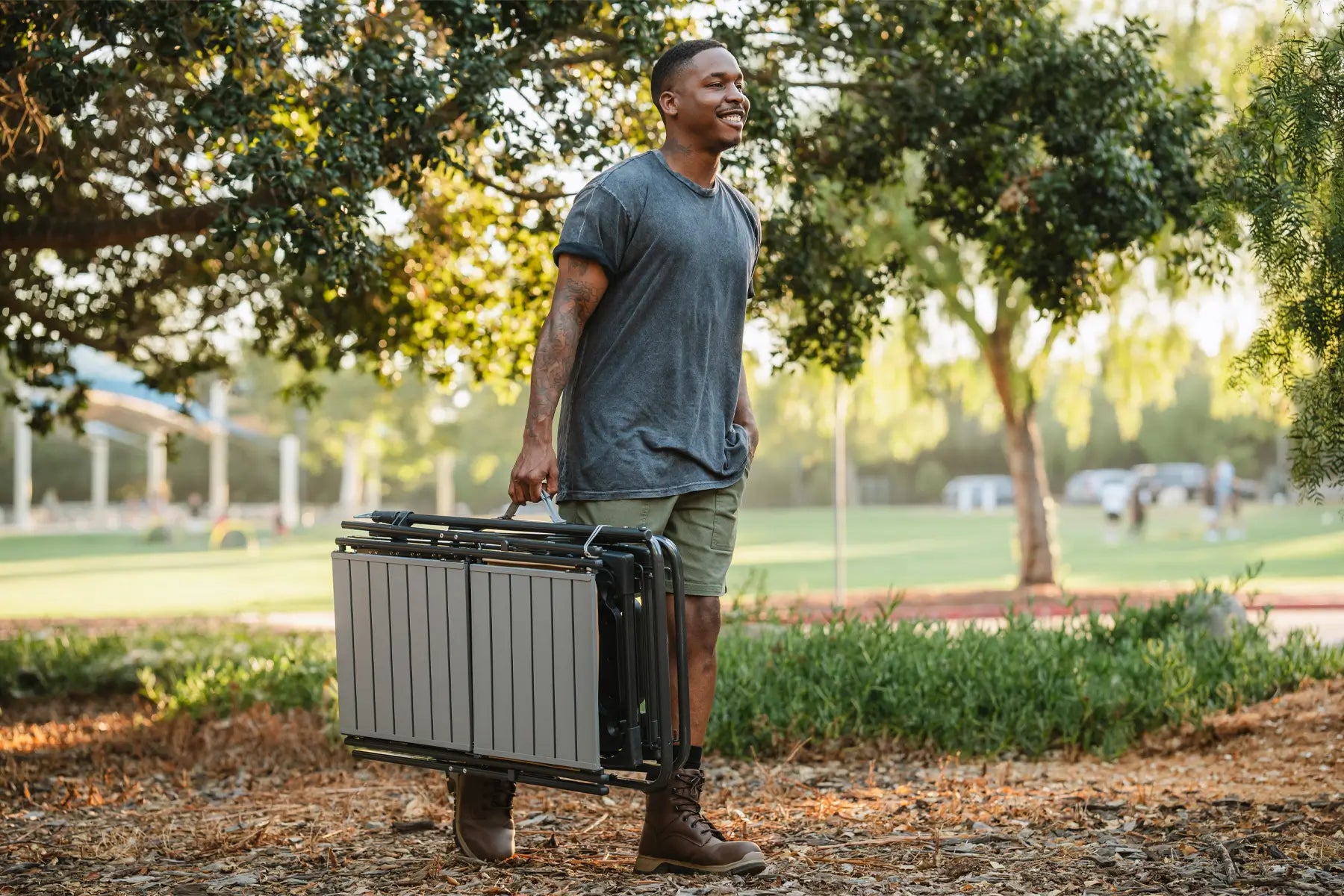 Man smiling while carrying the master cook station, surrounded by trees and sunlight.