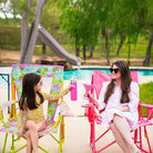 Girl and woman relax in colorful GCI Floral Comfort Pro Rocker chairs by a pool, raising their drinks in a playful toast.