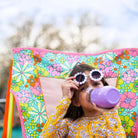Girl wearing daisy sunglasses drinks from a purple bottle while sitting in a floral-patterned GCI Comfort Pro Rocker.