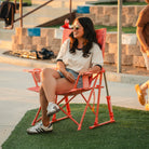 Woman laughing outdoors in a GCI Outdoor Comfort Pro Rocker in Coral Garden, front left angle view.