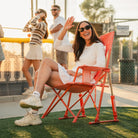 Woman waving and smiling at a softball game in a GCI Outdoor Comfort Pro Rocker in Coral Garden, front left angle view.